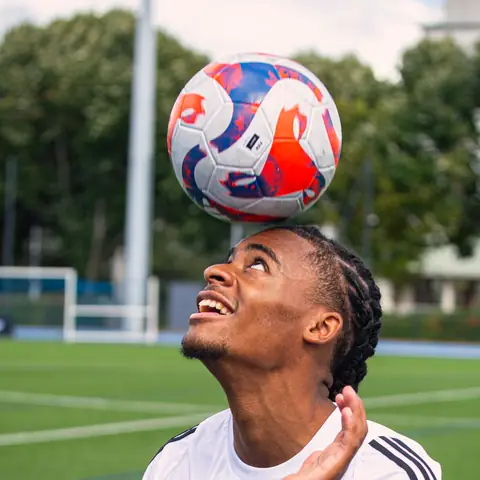A young player balancing a ball on his head, looking up at it.